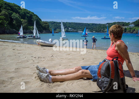 Une femme regardant des activités de voile dans l'estuaire de Salcombe au large de Mill Bay, une plage de sable abritée, populaire auprès des touristes et des habitants. Devon, Royaume-Uni Banque D'Images