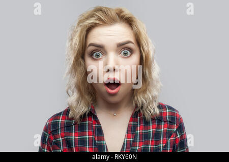 Closeup portrait of beautiful blonde woman in casual chemise à carreaux rouge debout avec de grands yeux et à la caméra et au visage surpris. Banque D'Images