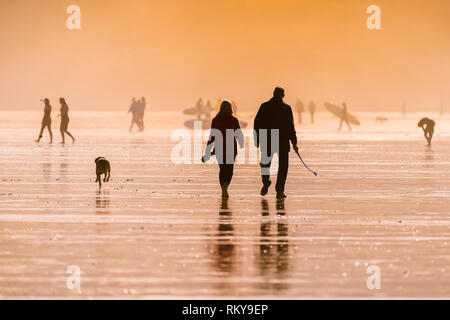 Les gens marcher leur chien sur la plage de Fistral dans la lumière du soleil de fin de soirée. Banque D'Images