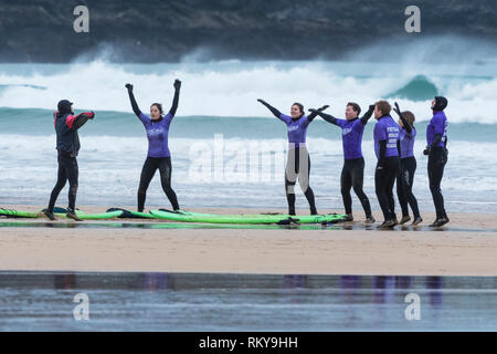 Les surfeurs débutants se réchauffer avec leur moniteur au début d'une leçon de surf à la plage de Fistral à Newquay en Cornouailles. Banque D'Images