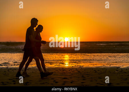 La silhouette d'un couple marcher le long de Torrey Pines State Beach en Californie comme le soleil se couche derrière l'océan Pacifique. Banque D'Images