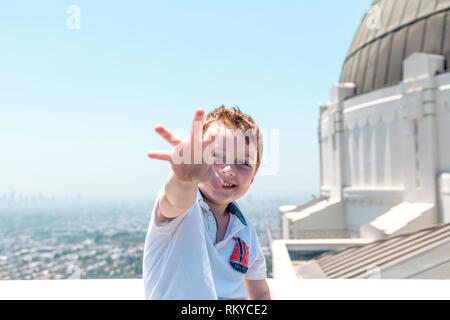 Jeune garçon aux cheveux rouge rire et atteindre vers la caméra avec l'Observatoire de Griffith et Los Angeles skyline derrière lui. Banque D'Images