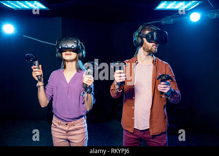 L'homme et de la femme joue une partie de l'utilisation de casque de réalité virtuelle et les manettes de jeu dans l'obscurité de la chambre club de lecture Banque D'Images