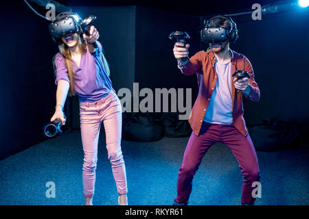 L'homme et de la femme joue une partie de l'utilisation de casque de réalité virtuelle et les manettes de jeu dans l'obscurité de la chambre club de lecture Banque D'Images