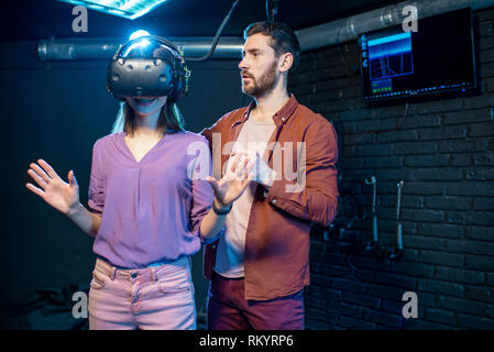 Jeune femme essayant casque de réalité virtuelle avec l'article avec l'homme assistant dans le club de lecture Banque D'Images