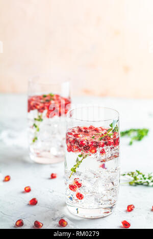 Boissons de fête, gin tonic cocktail de grenade ou de l'eau avec de la glace. detox Focus sélectif, l'espace de copie de texte, de la surface de la table en béton gris clair. Banque D'Images