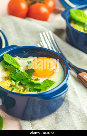 Oeufs cocotte kokot petit-déjeuner français. Oeufs cuits en bleu moules de cuisson en céramique. Cocotte de légumes et portionné oeufs dans le style italien. Banque D'Images