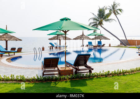 Des chaises longues et des nuances sous les palmiers autour de la piscine en plein air Banque D'Images