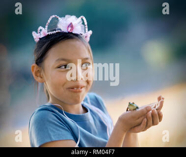 Jeune fille portant une couronne et tenant une grenouille verte dans ses mains. Banque D'Images