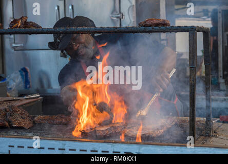 Man cooking steaks sur un barbecue avec des flammes et de la fumée. Banque D'Images