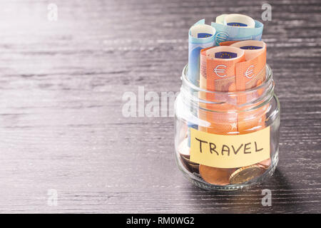 Bocal en verre avec des pièces et billets en euros avec le mot billet sur une table en bois noir. Concept de l'épargne financière pour une grande aventure de vacances. Banque D'Images