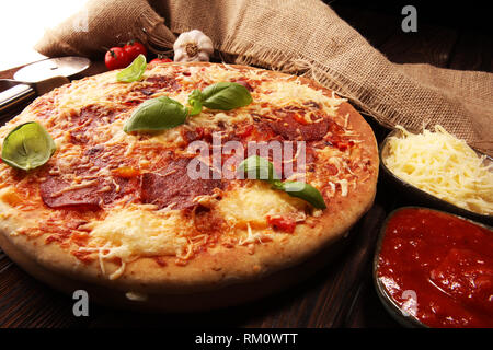 Italian Pizza au salami, peperoni - avec fromage fondu, tomates et basilic rouge vert sur une table décorée par du fromage, tomate et tomates cerises rouges Banque D'Images