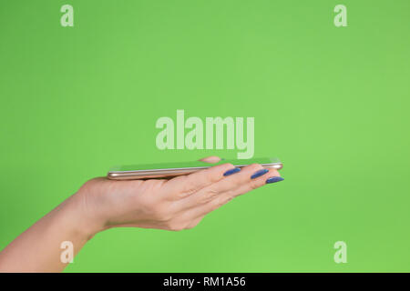 Vue latérale d'un gros plan femme part avec belle manucure bleu holding smartphone moderne avec un écran vert sur sa paume. Couleur horizontal phot Banque D'Images