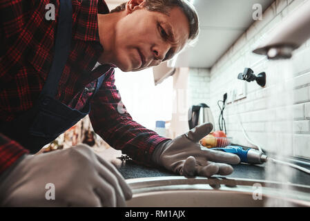 Vue de l'intérieur. Close-up of handsome plumber repairing sink en cuisine. Photo de l'évier et l'homme en métal avec tournevis Banque D'Images