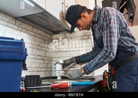 Robinet électrique. Vue arrière du beau plumber repairing sink en cuisine avec boîte à outils Banque D'Images