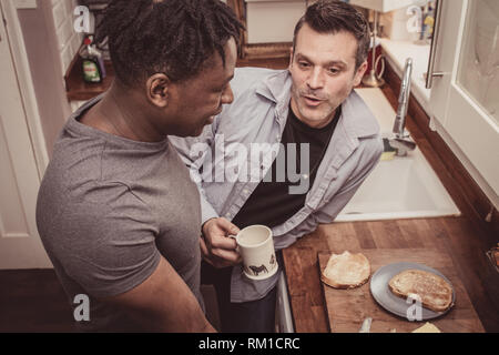 Un couple gay, partage les histoires de leur journée au travail sur une tranche de pain grillé et une tasse de thé et café dans la soirée. Banque D'Images