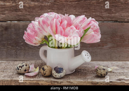 Carte de vœux de printemps. Oeufs de Pâques fleurs bouquet de tulipes fraîches rose petit jouet arrosoir vase sur fond de bois minable rustique. Concept de Pâques. Cop Banque D'Images