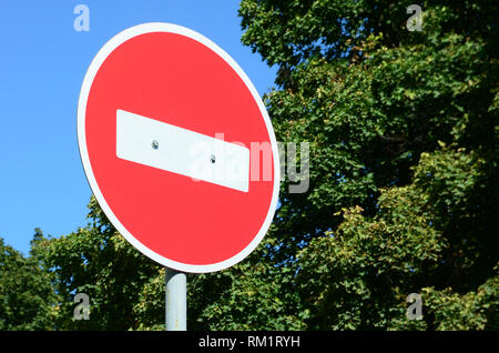 Une circulaire panneau rouge avec une barre blanche indiquant pas d'entrée sur un métal gris contre un des arbres vert et bleu ciel clair Banque D'Images