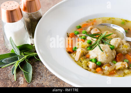 Soupe au poulet fait maison avec des légumes frais et des boulettes faites maison servi dans un bol blanc avec salières et poivrières et herbes fraîches. Banque D'Images