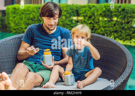 Père et fils manger le dessert avec chia seeds et de mangues à la piscine le matin. la saine alimentation, l'alimentation, les régimes végétariens et personnes concept Banque D'Images