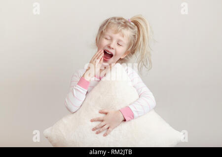 Concept un sommeil sain. Cute blonde woman enfant en pyjama rose avec les yeux fermés de bâiller large bouche ouverte à Palm. Sleepy kid avec m Banque D'Images