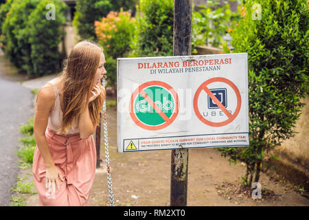 BALI, INDONÉSIE - 21 mai, 2018 : Jeune femme regarde signe de protestation sur un mur en indonésien s'opposer à l'Uber et saisir les chauffeurs de taxi se lit 'Uber et saisir Banque D'Images