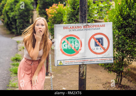 BALI, INDONÉSIE - 21 mai, 2018 : Jeune femme regarde signe de protestation sur un mur en indonésien s'opposer à l'Uber et saisir les chauffeurs de taxi se lit 'Uber et saisir Banque D'Images