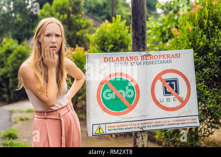 BALI, INDONÉSIE - 21 mai, 2018 : Jeune femme regarde signe de protestation sur un mur en indonésien s'opposer à l'Uber et saisir les chauffeurs de taxi se lit 'Uber et saisir Banque D'Images