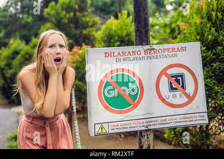 BALI, INDONÉSIE - 21 mai, 2018 : Jeune femme regarde signe de protestation sur un mur en indonésien s'opposer à l'Uber et saisir les chauffeurs de taxi se lit 'Uber et saisir Banque D'Images