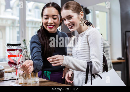 Belle Brunette femme asiatique dans un col polo marine et son ami discuter de nouveaux parfums Banque D'Images