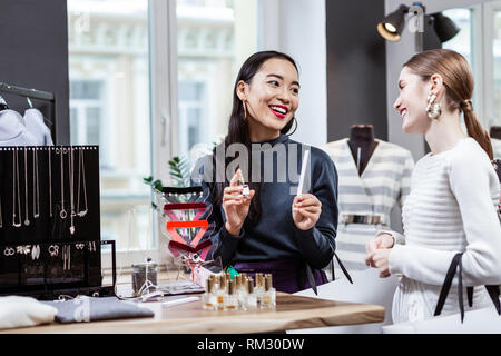 Dark-haired smiling asian woman in a marine polo cou présentant une nouvelle fragrance Banque D'Images