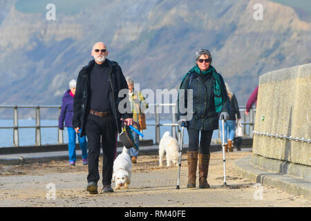 West Bay, Dorset, UK. 13 février 2019. Météo britannique. Soleil voilé se réchauffe dog walkers qui marchent le long de la promenade de West Bay, dans le Dorset qui sont enveloppés bien après froide pour commencer la journée. Les températures sont à la hausse que les vents des tropiques sont mis à souffler dans l'ensemble du pays au cours des prochains jours réunissant des températures au-dessus de la moyenne. Crédit photo : Graham Hunt/Alamy Live News Banque D'Images