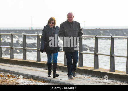 West Bay, Dorset, UK. 13 février 2019. Météo britannique. Soleil voilé se réchauffe les randonneurs qui marchent le long de la promenade de West Bay, dans le Dorset qui sont enveloppés bien après froide pour commencer la journée. Les températures sont à la hausse que les vents des tropiques sont mis à souffler dans l'ensemble du pays au cours des prochains jours réunissant des températures au-dessus de la moyenne. Crédit photo : Graham Hunt/Alamy Live News Banque D'Images