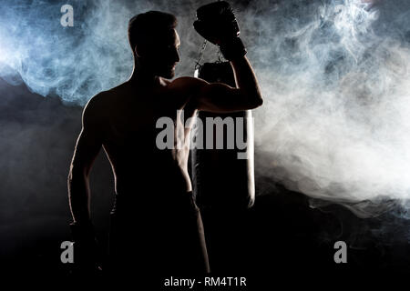 Silhouette de sportif musculaire dans des gants de boxe sur noir de fumée Banque D'Images