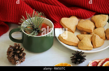 Composition chaude sur la table, une écharpe rouge, oranges séchées, les cookies en forme de cœur, une tasse de thé chaud avec une tranche de pamplemousse et de branches de pins Banque D'Images