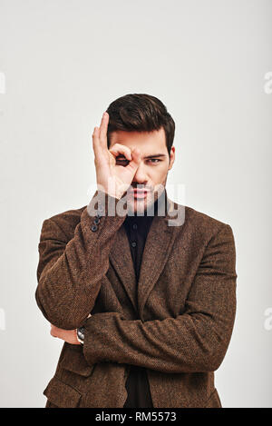 Portrait of a young man wearing jacket brown, looking at camera et faire OK S'identifier, isolé sur fond blanc. Concept de la réussite Banque D'Images