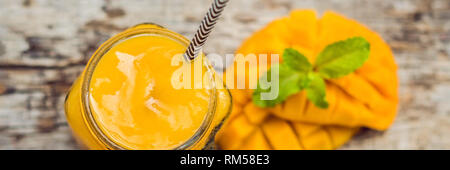 Smoothie mangue dans un verre pot Mason et de mangue sur un fond vert. Mango shake. Bannière concept fruits tropicaux, format long Banque D'Images