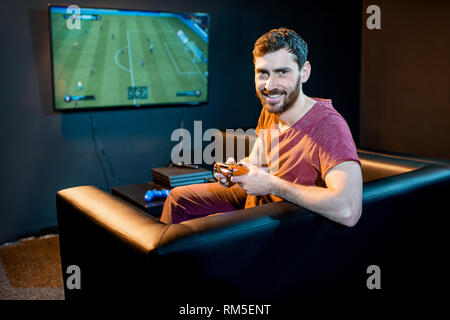 Portrait d'un homme heureux avec joy stick jouant au football jeu avec console de jeux assis sur le canapé à la lecture club Banque D'Images