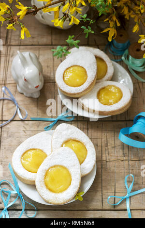 Composition de Pâques avec des cookies en forme d'œuf rempli de lait caillé de citron, lapin, bouquet de forsythia et d'arcs. Banque D'Images