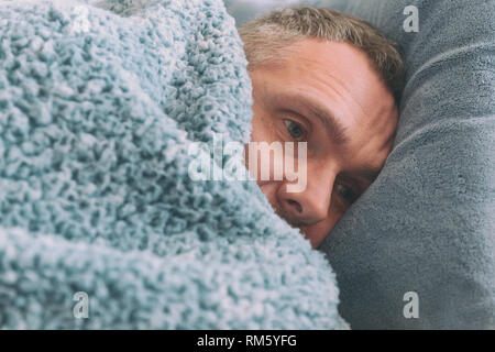 Homme mûr souffrant de dépression se trouve malheureusement recouvert d'une couverture sur son lit Banque D'Images
