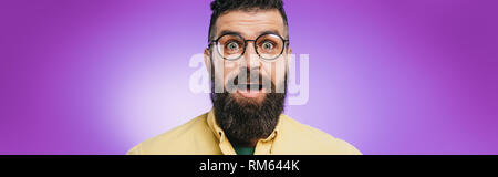 Homme barbu à lunettes choqué looking at camera, isolé sur purple Banque D'Images