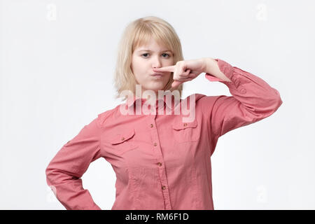 Femme blonde moustache montrant avec le doigt. Elle se sent mauvaise odeur. Banque D'Images