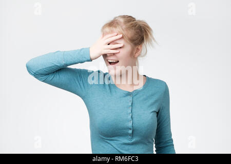 Happy young blonde woman standing sur fond gris et couvrant les yeux. Banque D'Images