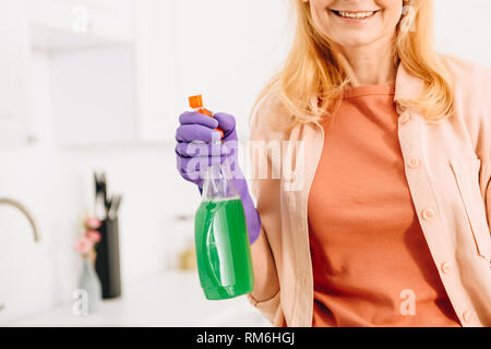 Portrait of smiling senior woman in rubber glove holding spray Banque D'Images