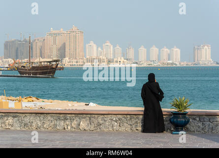 Scène de rue à Doha, au Qatar, avec dame portant Qatari traditionnelle robe noire et avec le chapeau de Pearl district gratte-ciel en arrière-plan. Banque D'Images