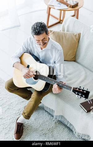 Vue de dessus de cheerful senior man playing acoustic guitar in living room Banque D'Images