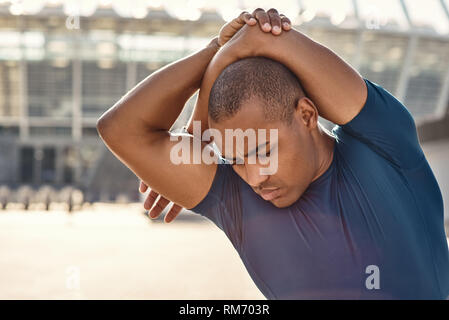 Sentez vos muscles. Close up portrait of athletic homme africain debout à l'extérieur et s'étendant ses bras avant la formation. Le Cardio-training. De saines habitudes de vie. Motivation sport concept. Concept de remise en forme. Banque D'Images