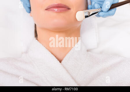 Portrait de l'application de masque de beauté cosmétiques femme cosmétiques sur le visage avec une brosse au salon de Banque D'Images