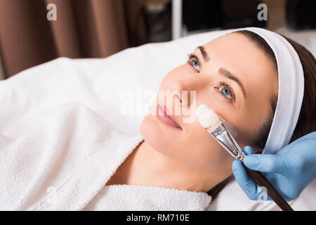 Début coiffeur d'appliquer un masque de beauté avec un pinceau pour femme sur le visage au salon de beauté Banque D'Images