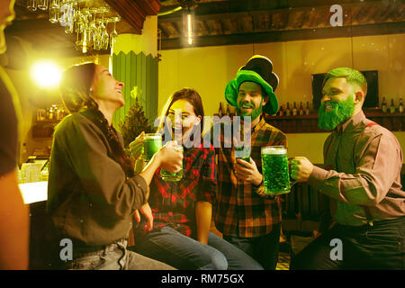 Saint Patrick's Day Party. Happy friends fête et boire la bière verte. Les jeunes hommes et femmes portant un chapeau vert. Pub de l'intérieur. Banque D'Images